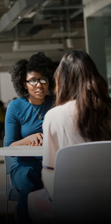 Duas mulheres sentadas à mesa, conversando animadamente em um ambiente acolhedor